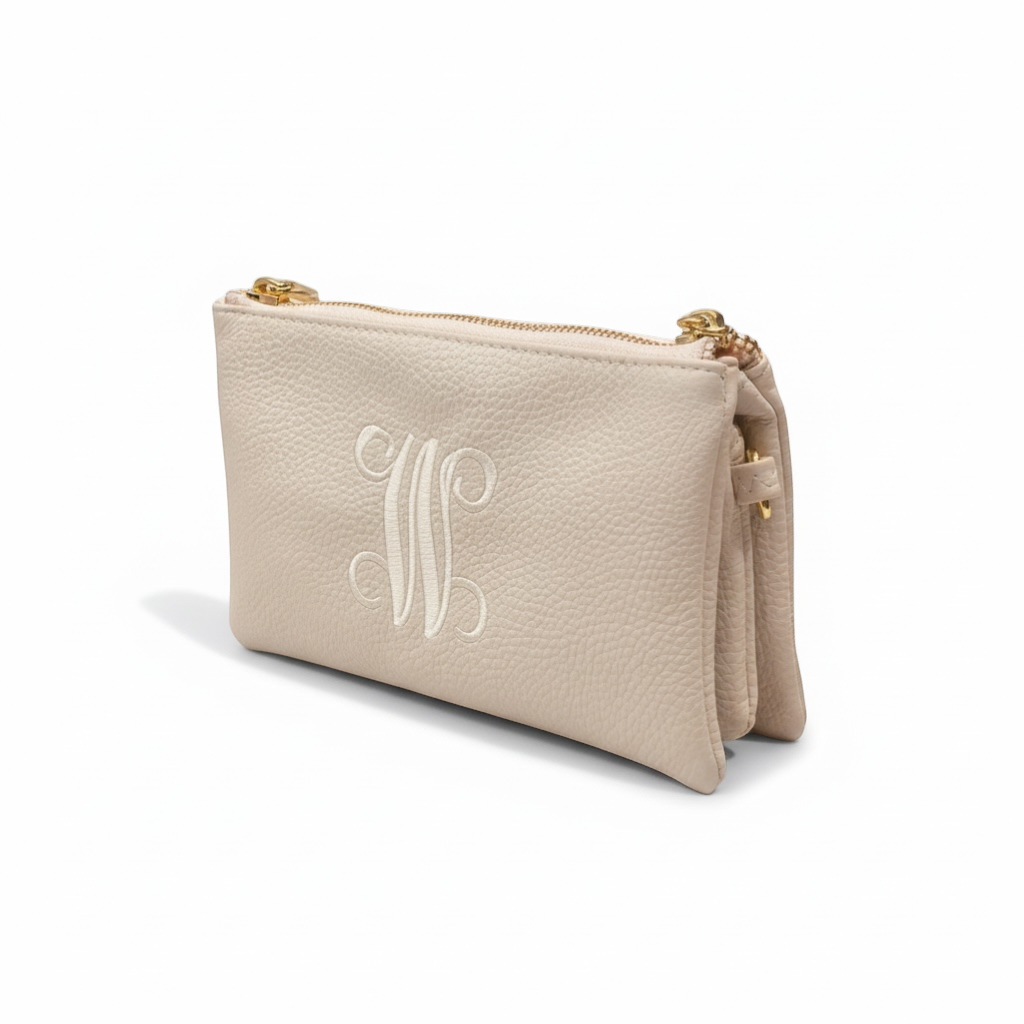 The Xchange beige pebbled leather clutch with embroidered monogram and gold zipper detail.