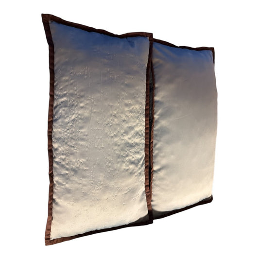 The Xchange set of two rectangular cream throw pillows with textured fabric and dark brown piped edges.