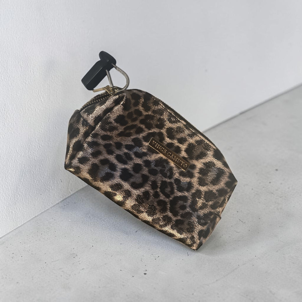 The Xchange Vince Camuto small makeup bag in a metallic leopard print with a gold logo plate and zip closure.
