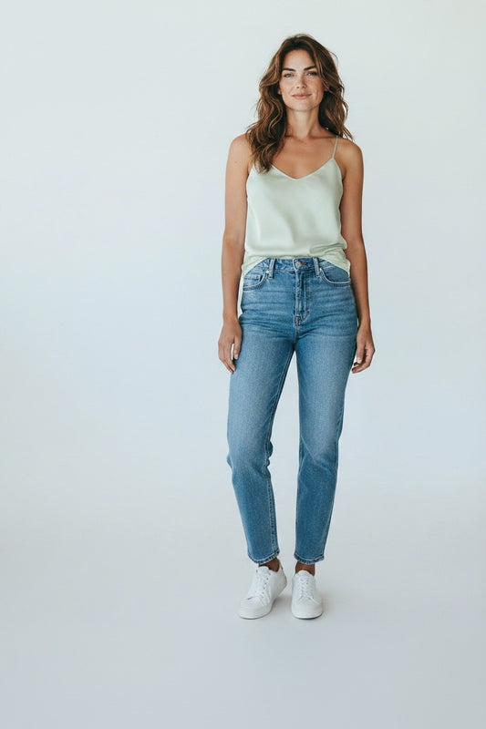 The Xchange pale green satin camisole with spaghetti straps and V-neckline worn by a model with high-rise straight leg jeans.